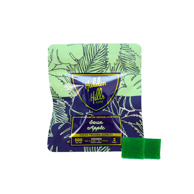 The "Hidden Hills Club" package features "500mg" and "1000mg" THC edibles, including a visible green gummy prominently displayed. Adorned with a leaf pattern on a green and purple background, these Hidden Hills Heady Blend Gummies | 2ct are crafted with high-quality cannabis extracts for an elevated experience.